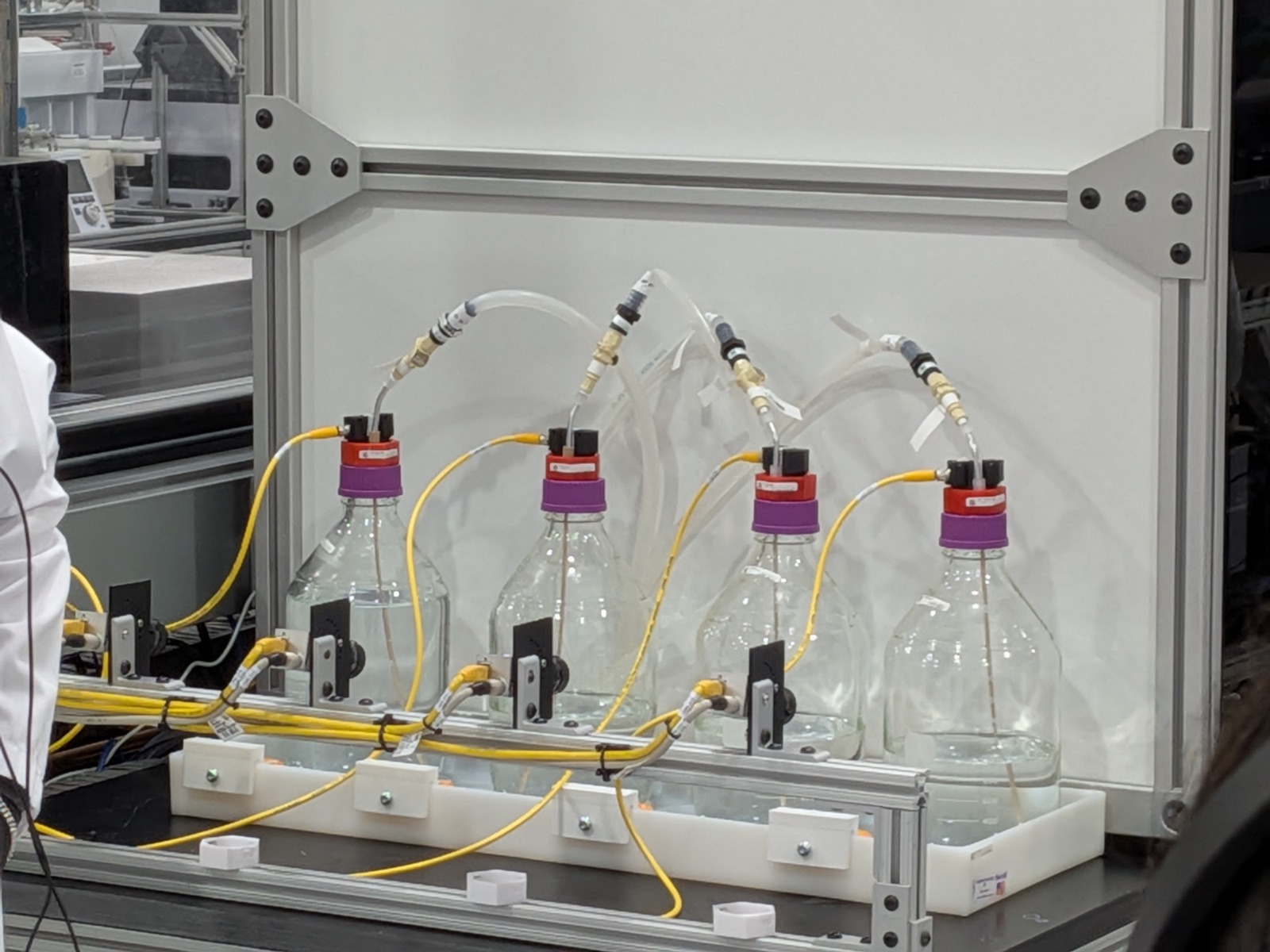 Four glass reagent bottles fitted with sensor caps and tubing, each monitored by its own dedicated machine-vision camera.